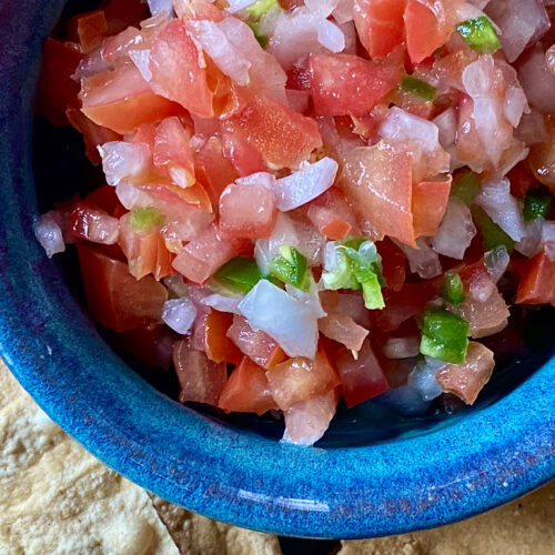 Close up Pico de Gallo in a blue pottery bowl with tortilla chips on the side