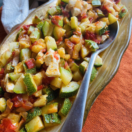 Calabacitas a la Mexicana on a golden platter with a metal spoon for serving.