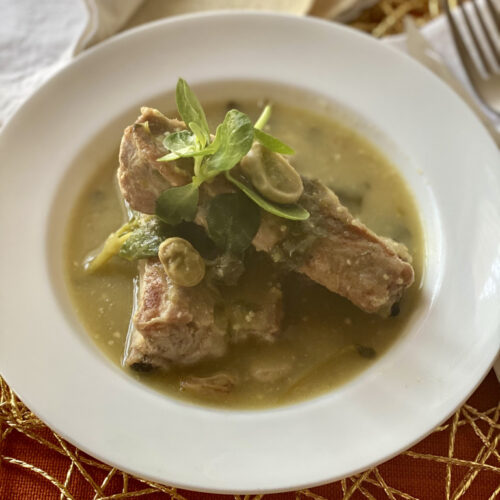 Close pork ribs in salsa verde in a white bowl on a gold and orange placemat