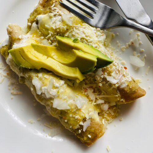 Close up of Enchiladas Suizas on a white plate with a fork and knife