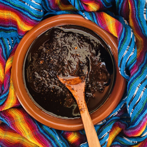 Salsa de Chile Pasilla in a pottery bowl with a wooden spoon, on top of a colorful Mexican rebozo