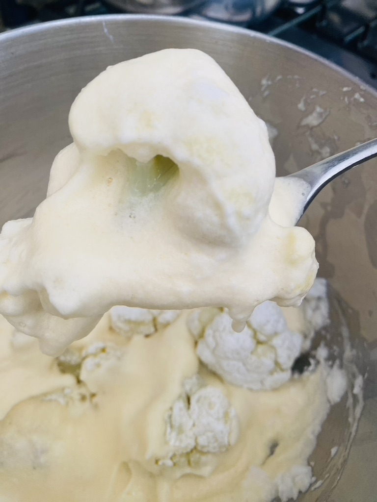 Cauliflower coated with egg batter on a spoon, ready for frying