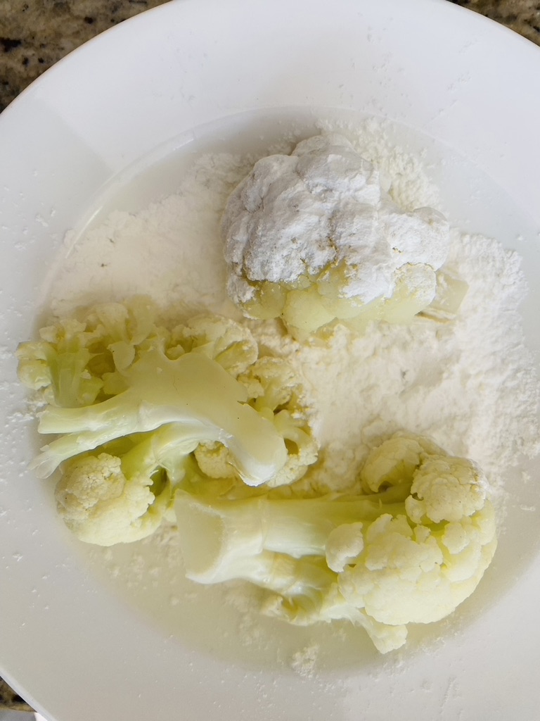 Pieces of cauliflower on a white plate being coated with flour