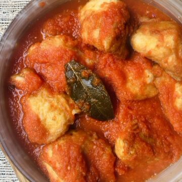 Cauliflower fritters in a golden bowl soaked in tomato-based sauce with a bay leaf on top
