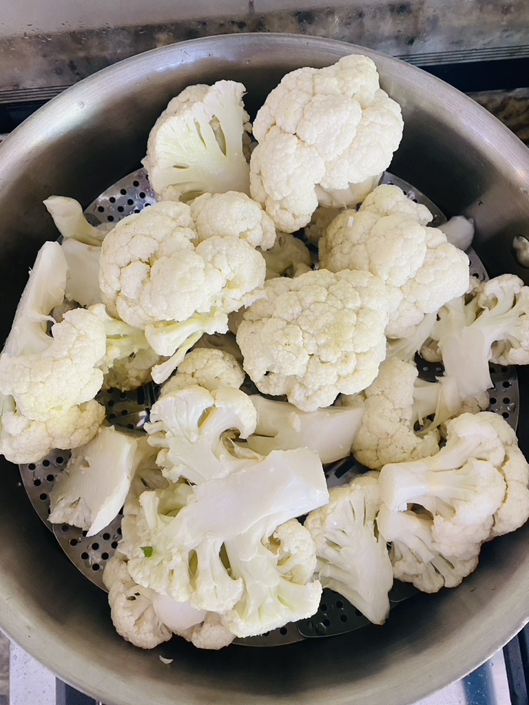 Cauliflower pieces in a steamer basket in a stainless steel pan on the stove
