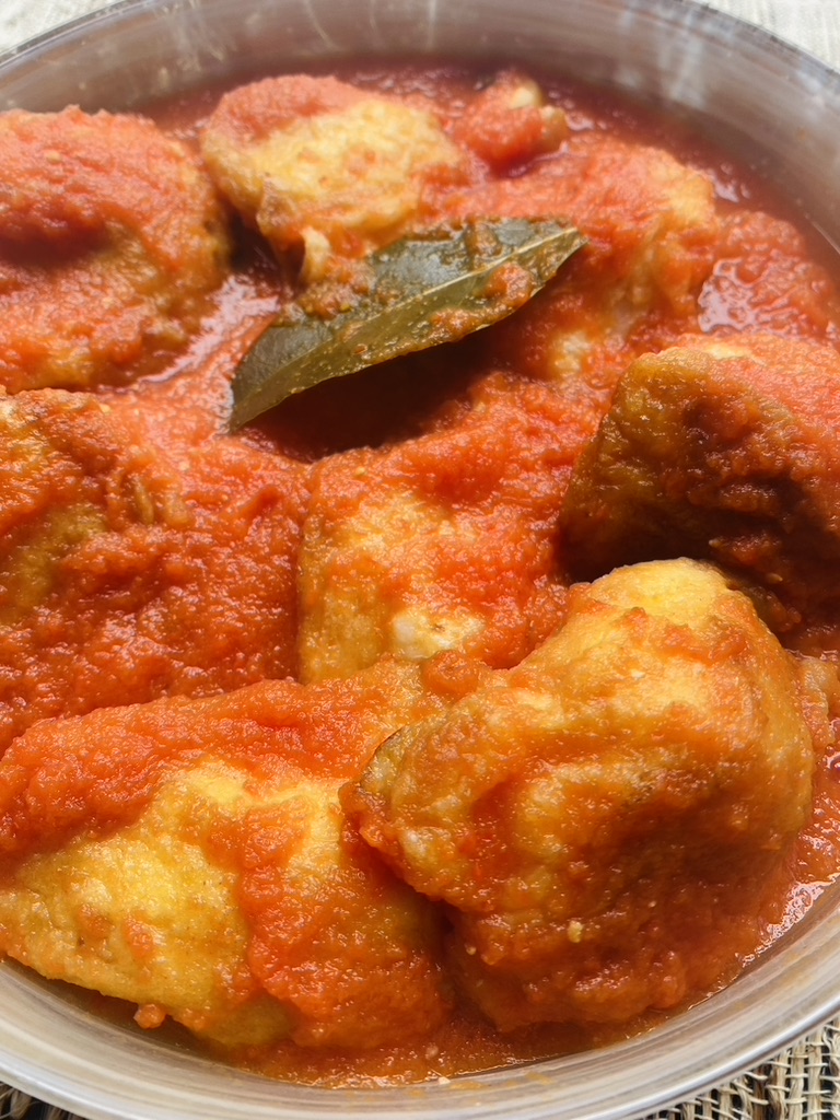 Close up of cauliflower fritters in tomato sauce with a bay leaf on top