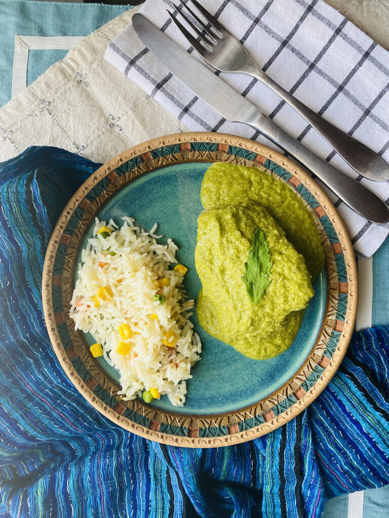 Mole verde with a whole chicken thigh on a blue potter plate with a side of rice