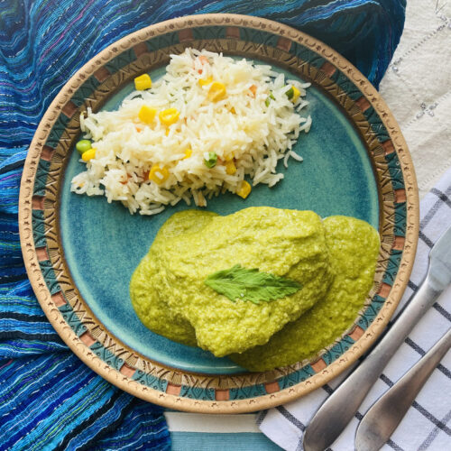 Mole Verde with Chicken and white rice, served on a blue pottery plate, with a fork and knife on the side