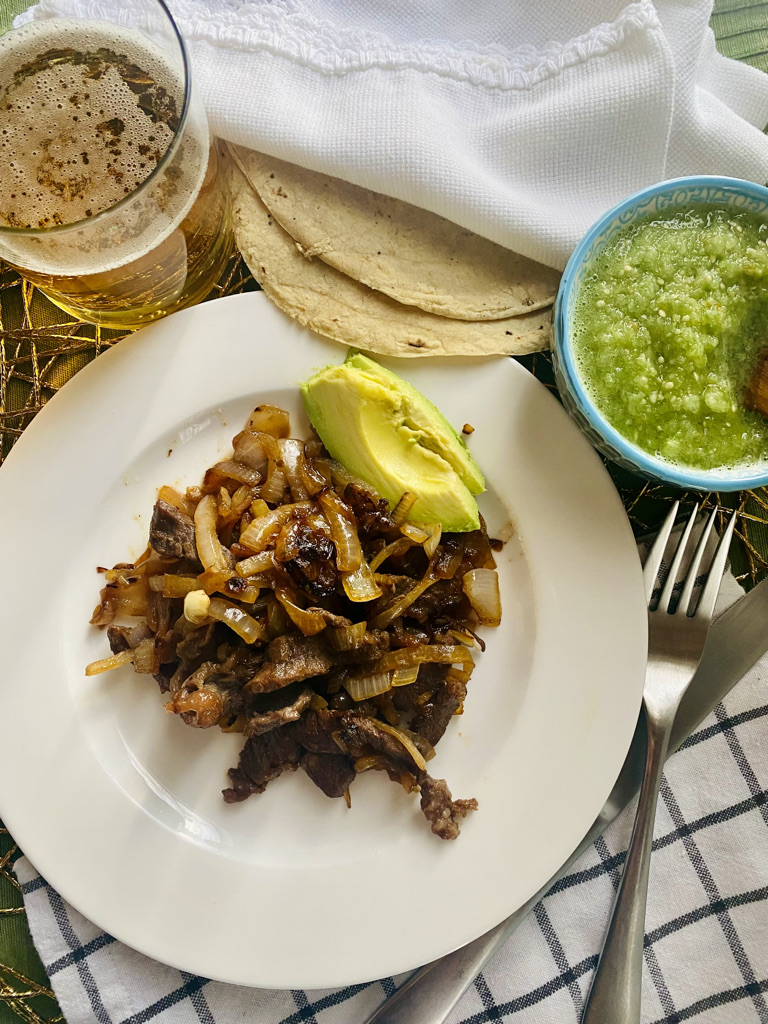 Plated bistec encebollado with salsa, beer, and tortillas