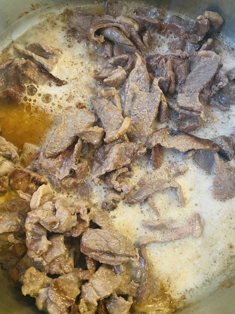 Strips of steak cooking in beer in a metal pan