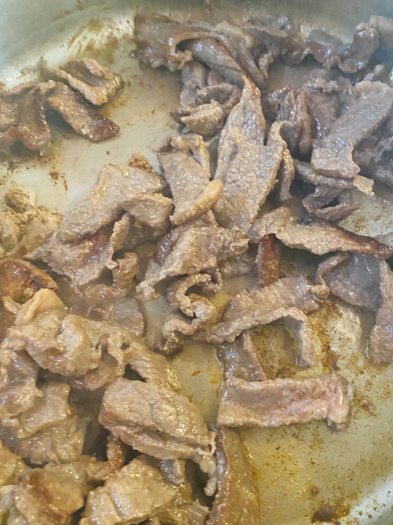 Strips of steak frying in a metal pan with oil