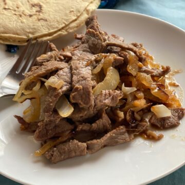 Plate of Mexican steak and onions with corn tortillas