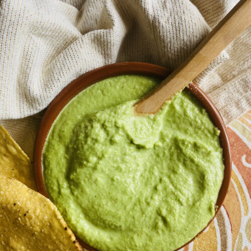 No cream, creamy jalapeño salsa served in a bowl, with tostadas and a wooden spoon