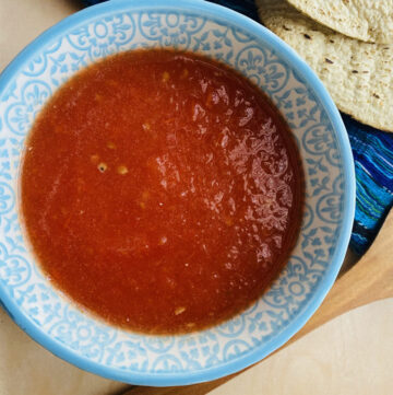 Yucatán-style tomato and habanero salsa in a blue and white bowl with tostadas and a wooden spoon on the side