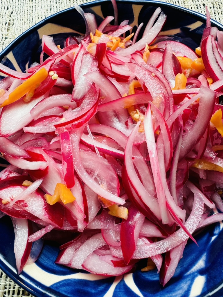 Red onion and habanero strips in a blue pottery bowl after pickling