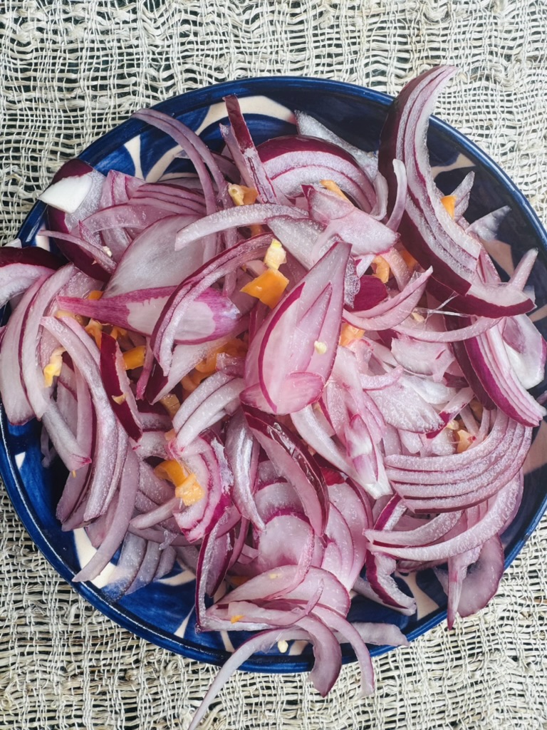 Red onion and habanero strips in a blue pottery bowl before pickling has begun