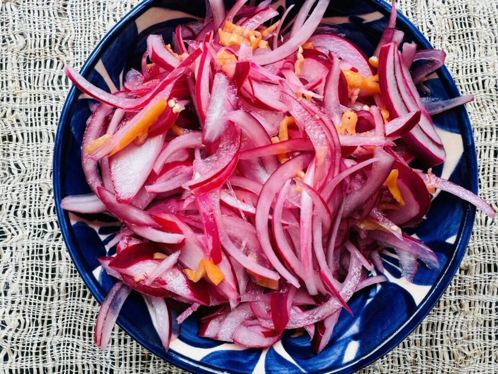 Sliced red onions, habaneros and lime juice in a blue pottery bowl