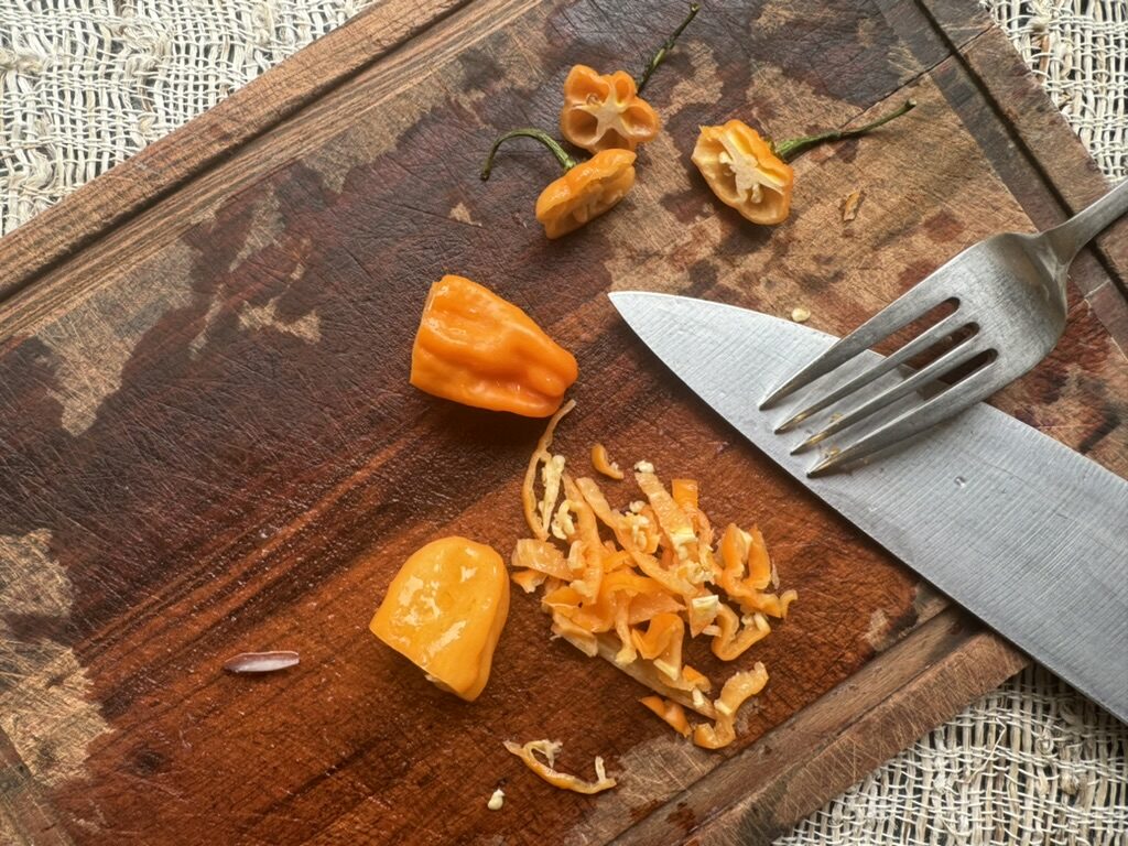 Habaneros being sliced on a wooden cutting board, fork and knife