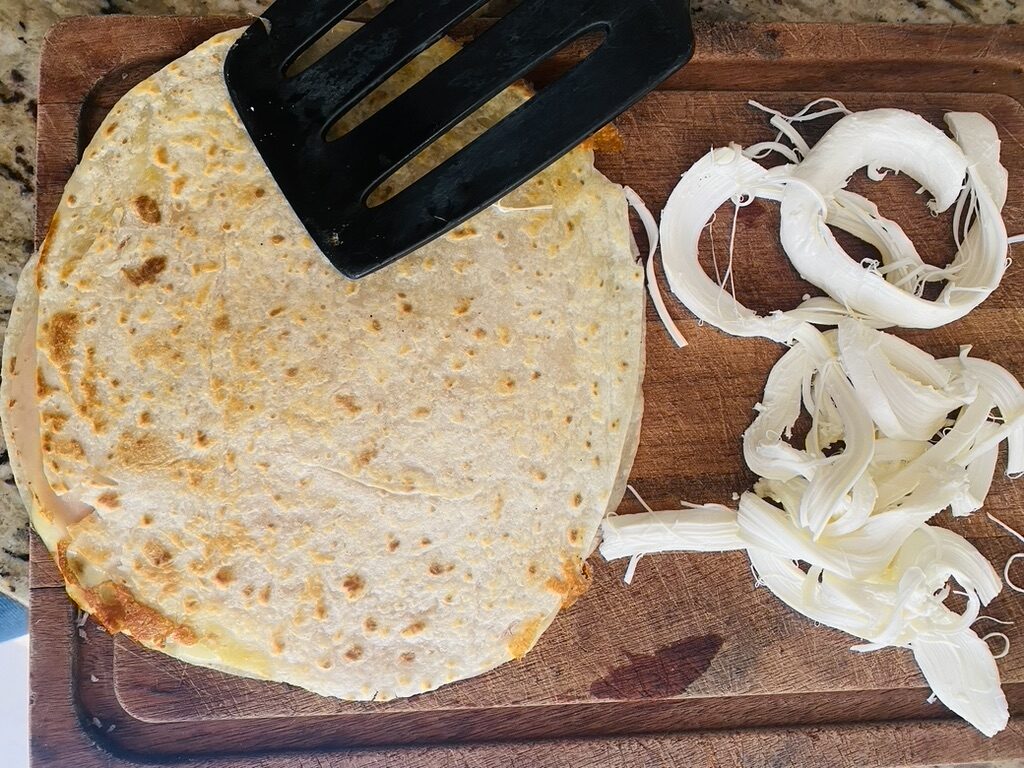 Finishes sincronizada and shredded Oaxacan cheese on a cutting board