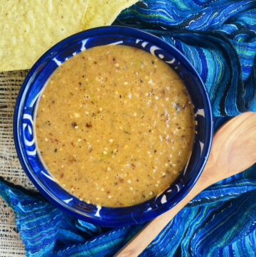 Chile morita and tomatillo salsa in a blue talavera bowl with a wooden spoon and tostadas on the side, blue rebozo in the background