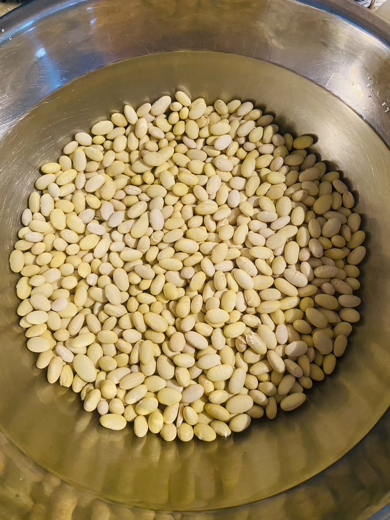 Dried beans soaking in water in a metal bowl
