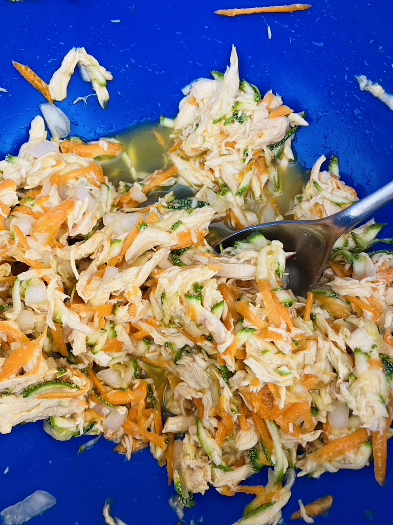 Blue bowl with shredded chicken, shredded Mexican grey squash, shredded carrots, and beaten eggs