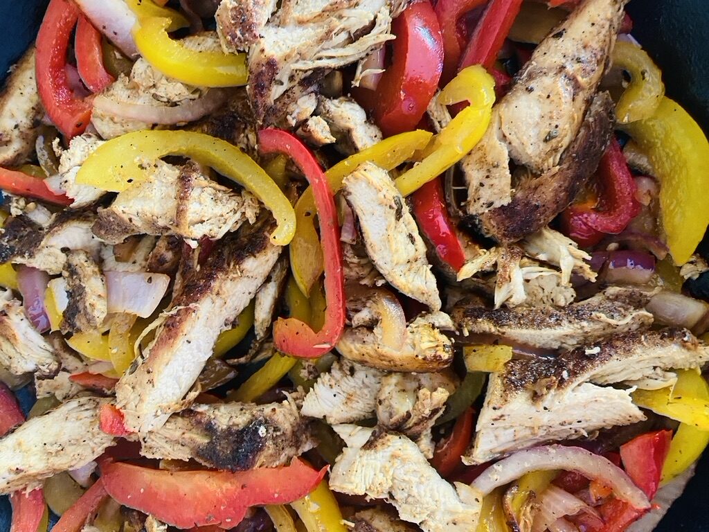 Chicken strips, thinly sliced onions, and bell pepper strips cooking in a non-stick skillet