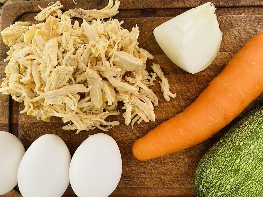 Chicken and vegetable fritter ingredients, eggs, shredded chicken, onion, carrot and Mexican grey squash on a cutting board