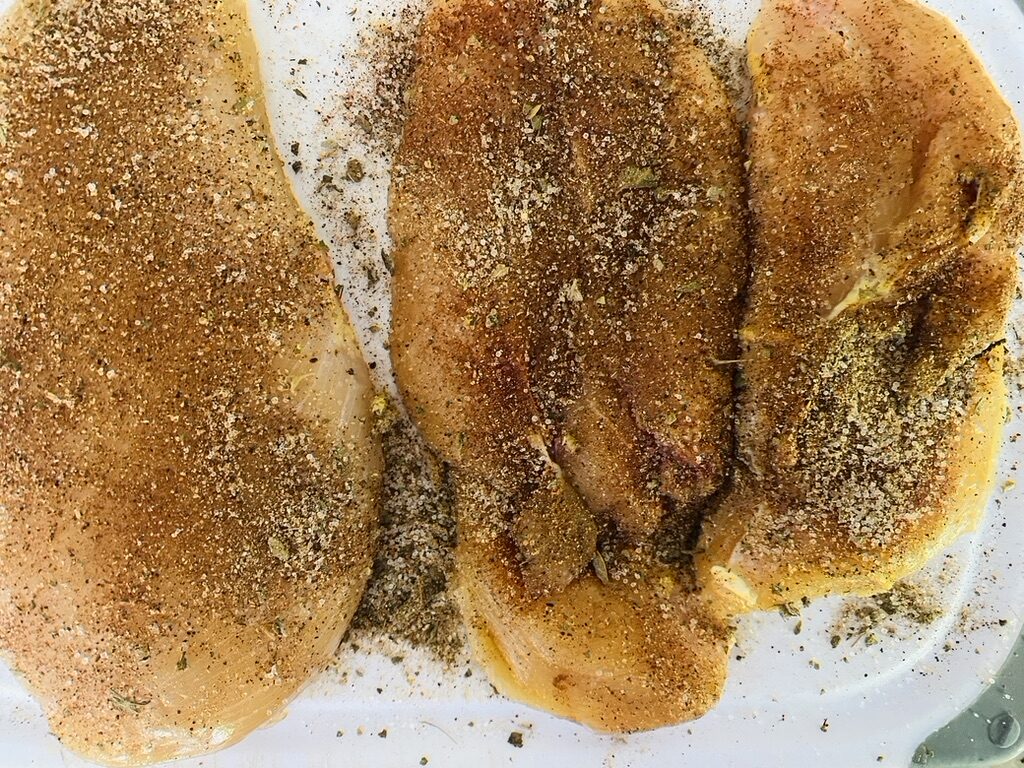 3 raw chicken breasts on a cutting board, rubbed with fajita spice mixture