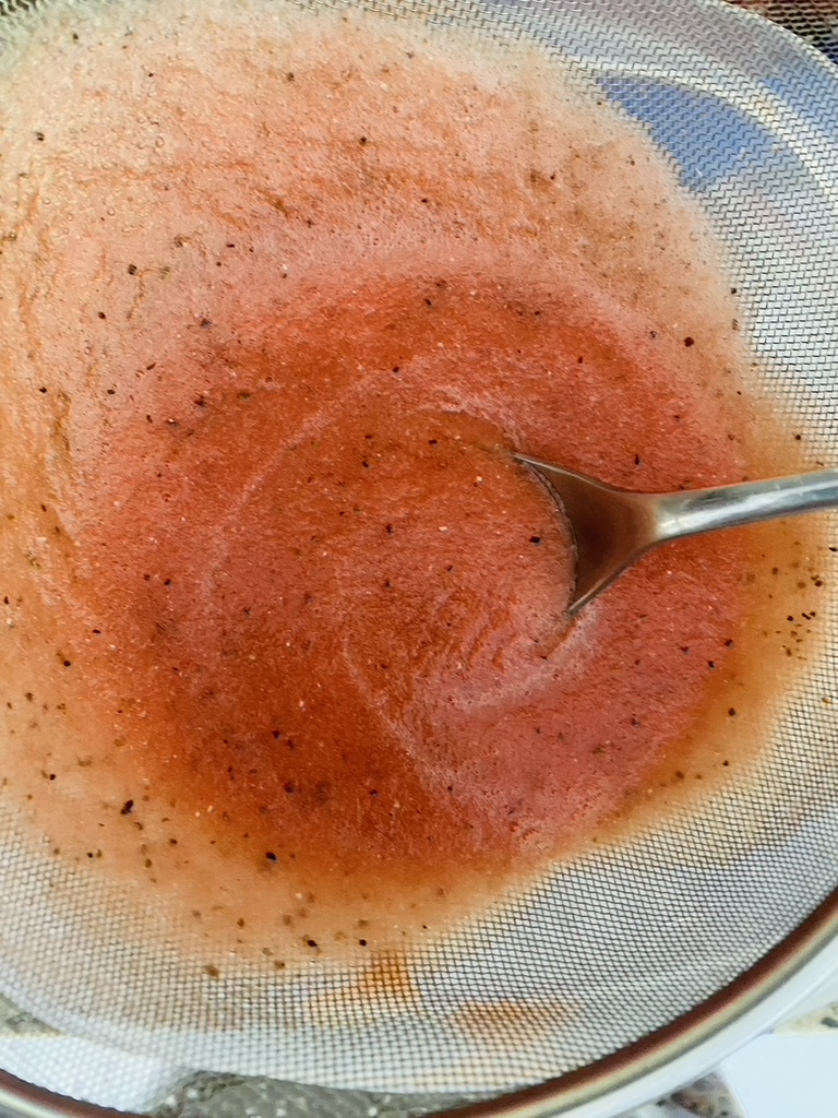 Watermelon juice being strained through a fine-meshed sieve