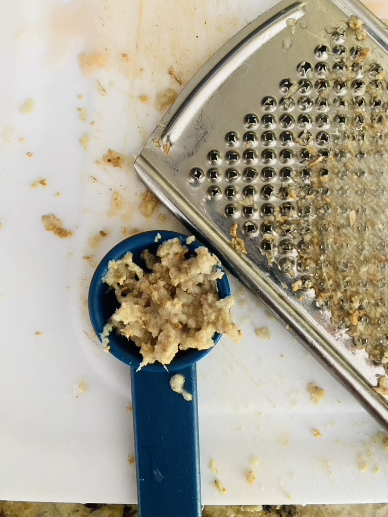 Grated ginger in a a measuring spoon with a grater 