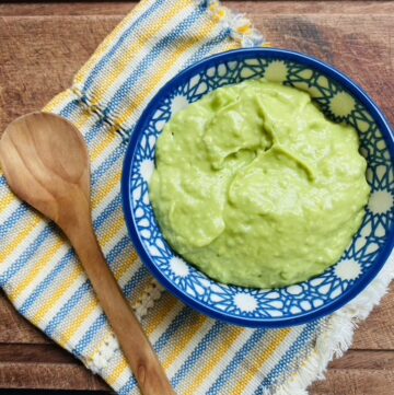 Creamy avocado salsa in a blue patterned bowl on top of a blue and yellow napkin