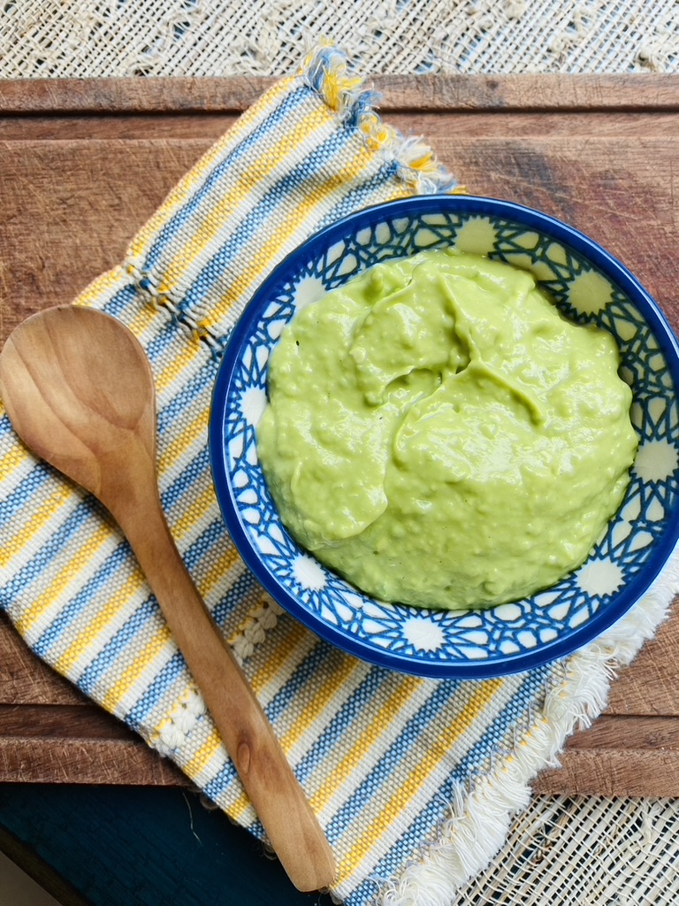 Creamy avocado salsa in a blue patterned bowl on top of a blue and yellow napkin