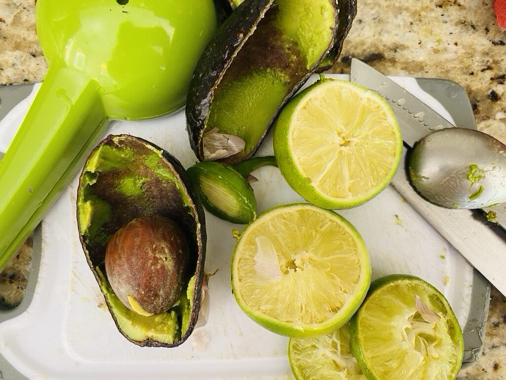 Squeezed limes, avocado skins, and jalapeño stem on top of a cutting board