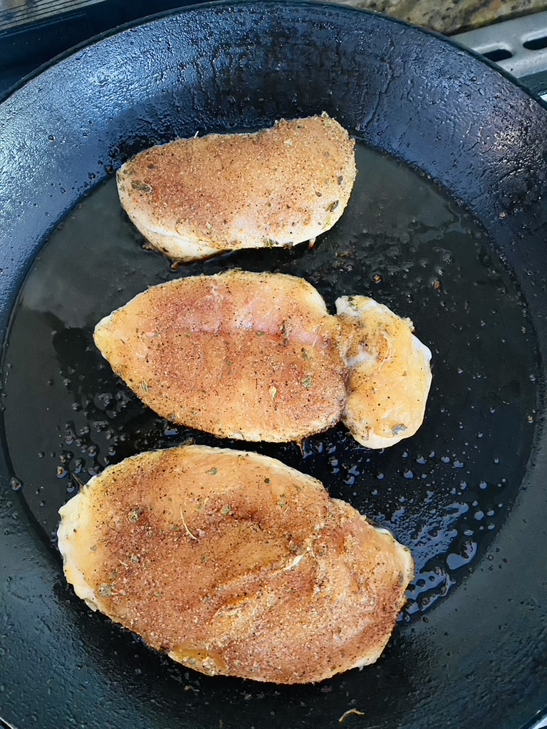 3 chicken breasts for fajitas cooking on the first side in a non-stick skillet