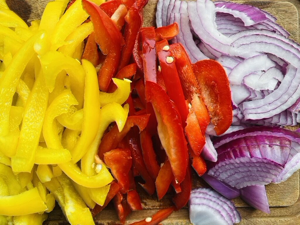 Strips of yellow and red bell pepper, and thin slices of red onion on a wooden cutting board