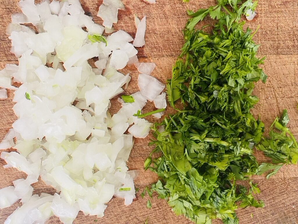 Wooden cutting board with finely diced white onion and chopped cilantro