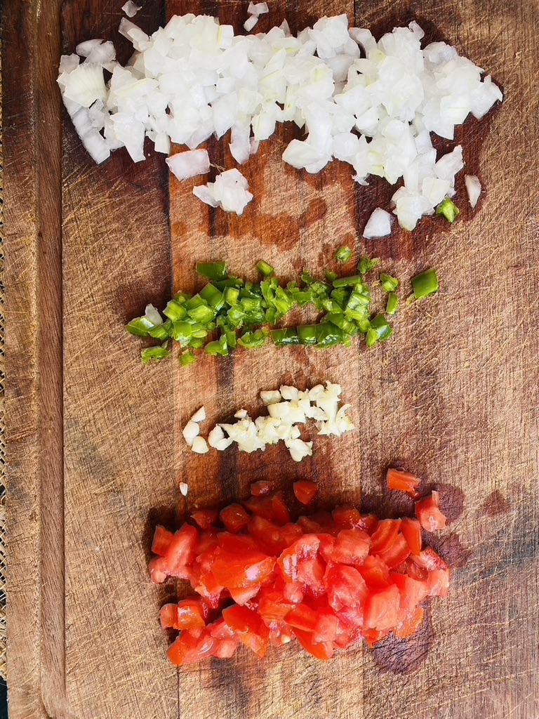 Chopped onion, serrano chile, garlic, and tomato on a wooden cutting board