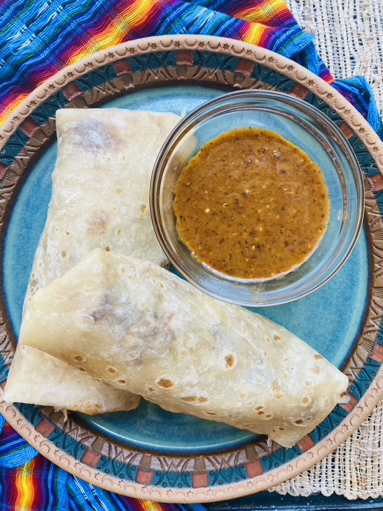 2 small breakfast burritos on a blue pottery plate with a side of chile morita salsa in a bowl