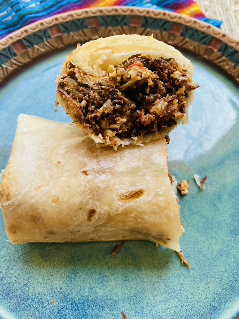 Close up of half a machaca and egg burrito on a blue pottery plate