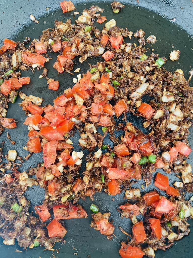 Machaca with tomatoes, onions, peppers, and garlic frying in a pan