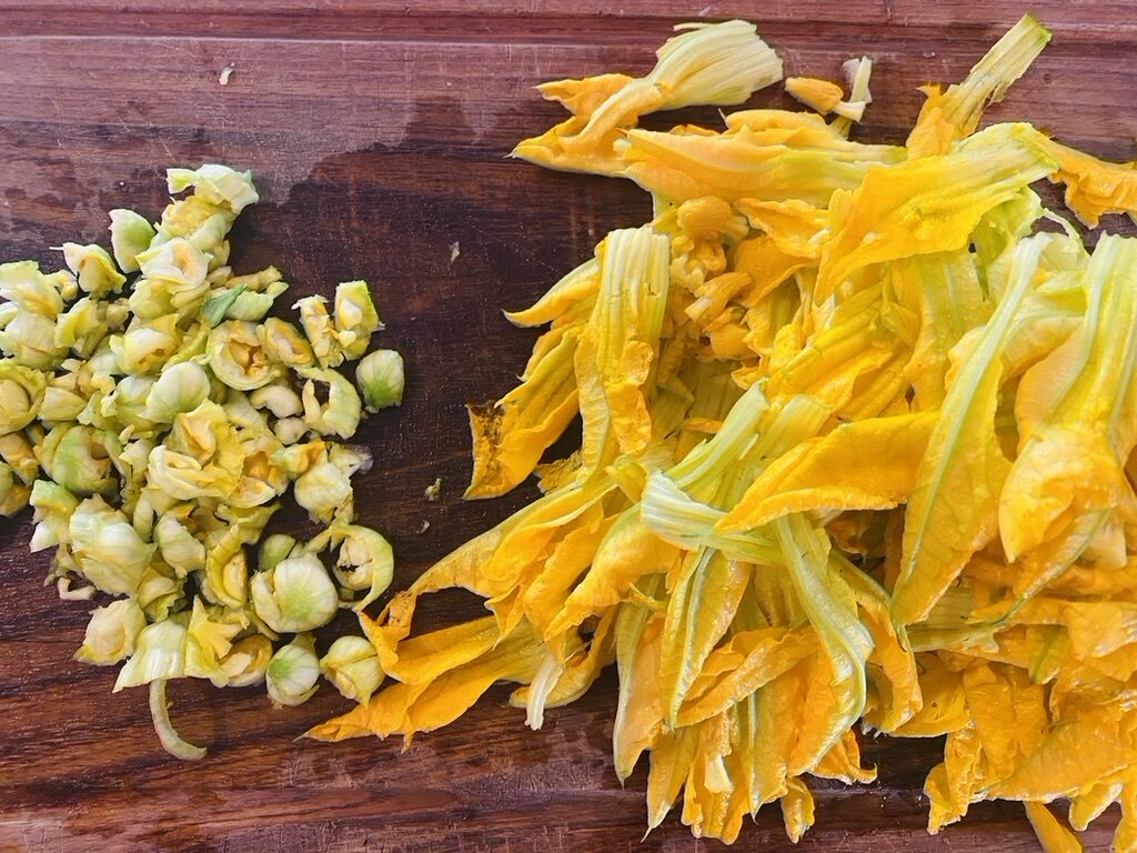 Wooden cutting board with chopped squash blossom chalices and flowers torn into strips