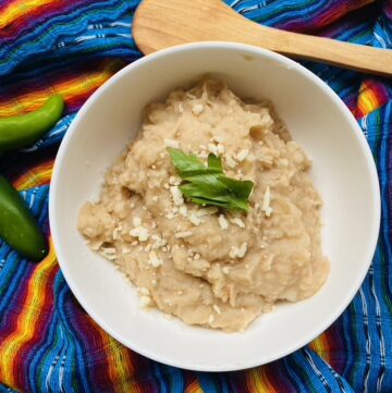 White bowl with refried beans topped with shredded cheese and cilantro