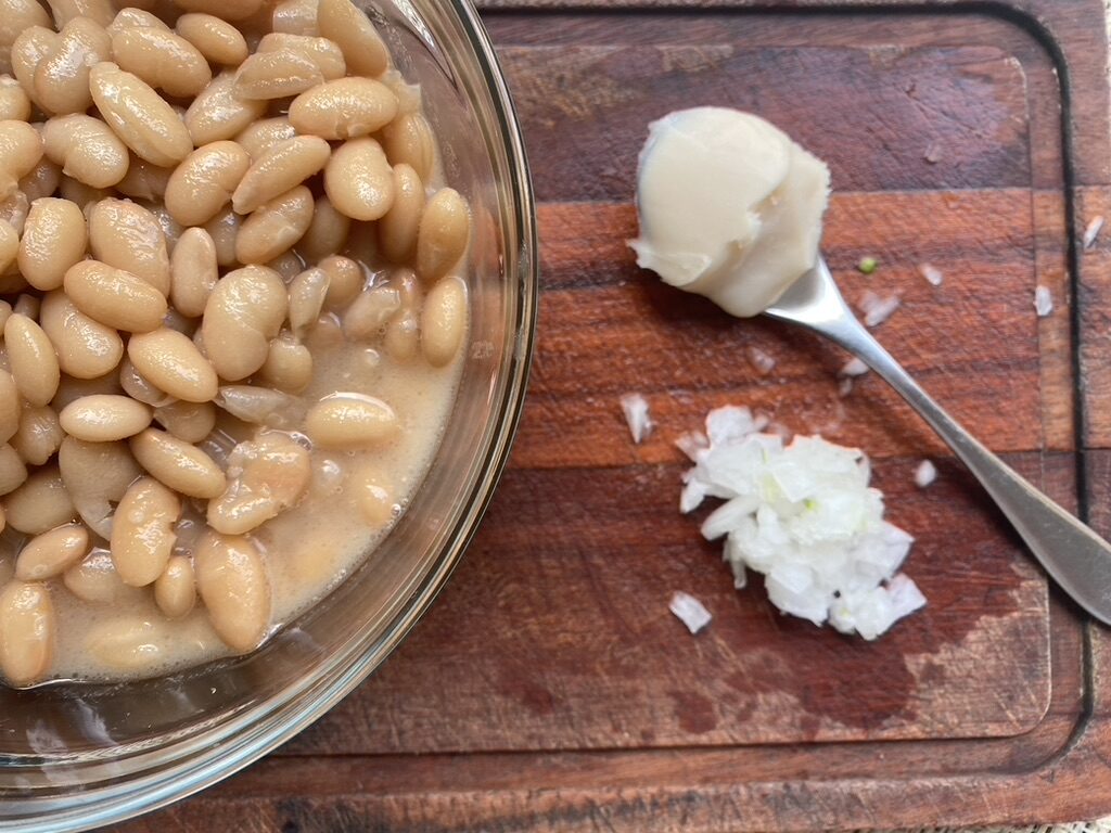 Wooden cutting board with bowl of Peruvian beans, diced onion, and a spoonful of lard