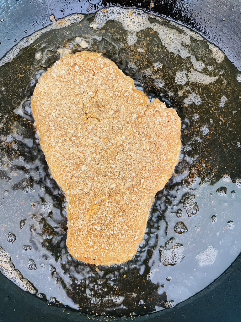 Breaded chicken milanesa frying in oil in a non-stick pan