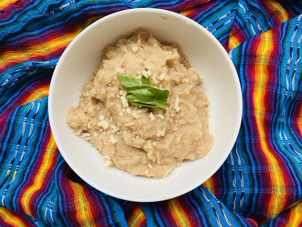 White bowl with refried beans, topped with shredded cheese and cilantro