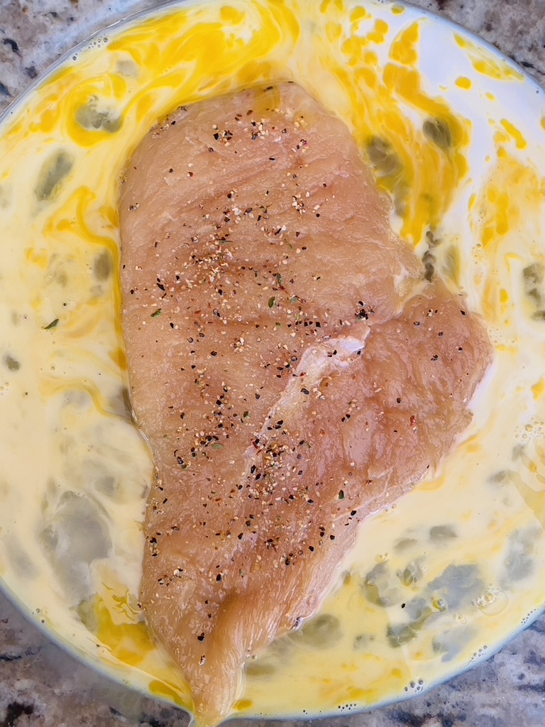 Seasoned chicken milanesa in a pie plate with a mix of egg and milk