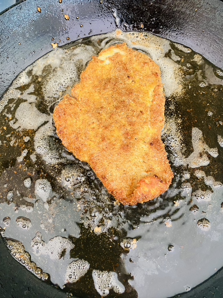 Milanesa that has been cooked on one side is frying in a non-stick pan to cook the other side