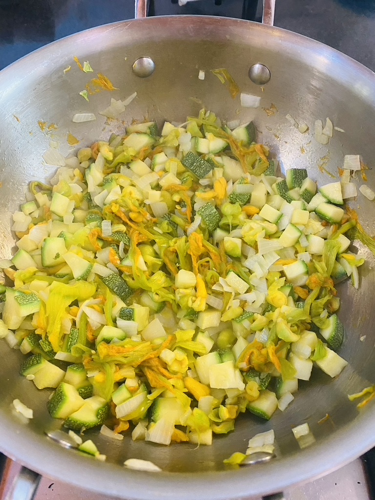 Soup pan with chopped squash, squash blossoms, and onion