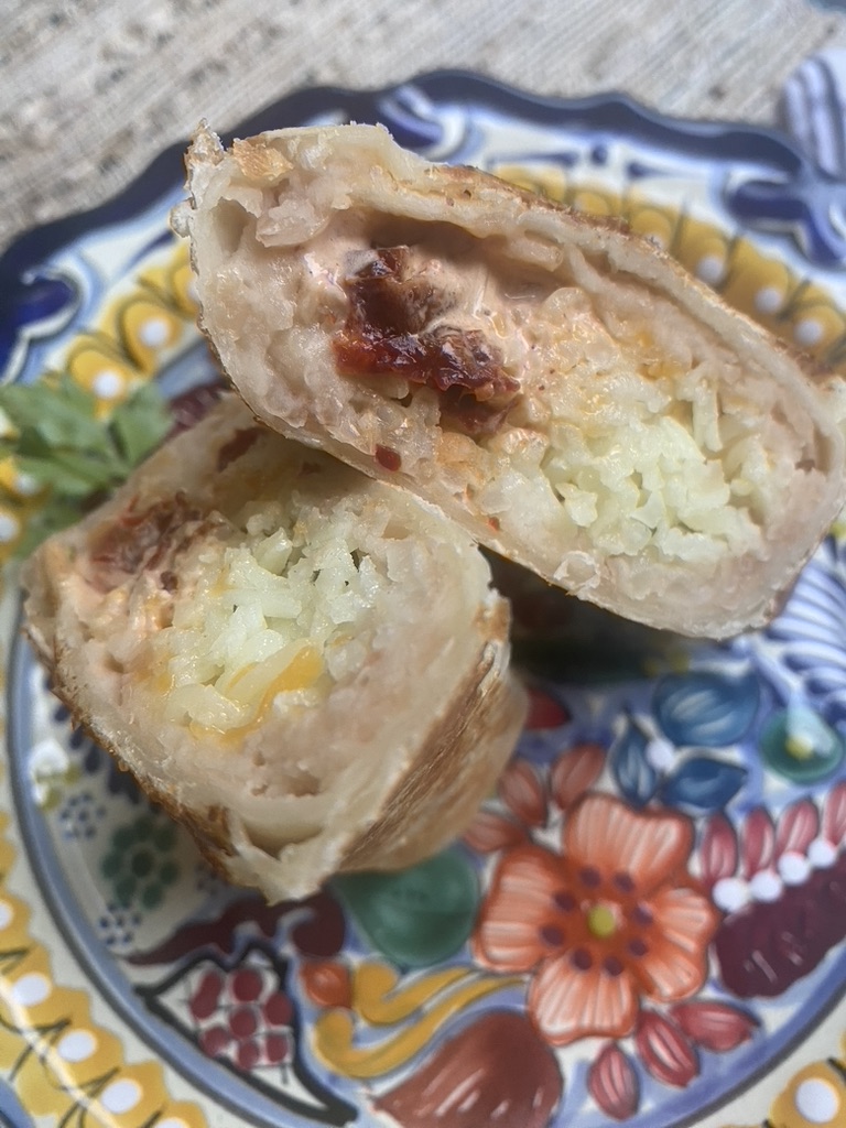 Close up of a bean, rice, cheese, and chipotle crema burrito cut in half on a Mexican talavera plate